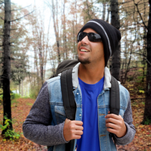 Un hombre lleva el gorro negro con franjas reflectantes mientras hace senderismo en el bosque con una mochila y una chaqueta abrigada