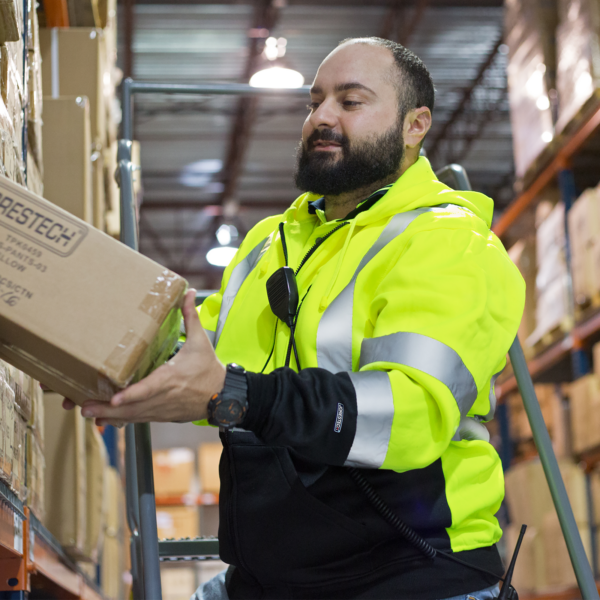 Un trabajador que lleva un suéter de seguridad amarillo de alta visibilidad clase 2 tipo R. Está retirando una caja de un contenedor en un entorno de almacén.
