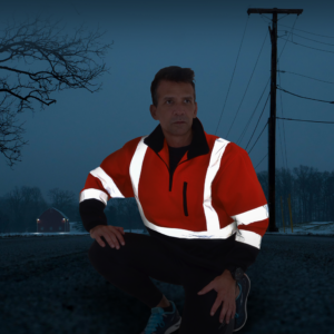 Un hombre lleva el suéter de seguridad JORESTECH de alta visibilidad durante la noche, mostrando la luz reflejada en las franjas reflectantes para aumentar la visibilidad.