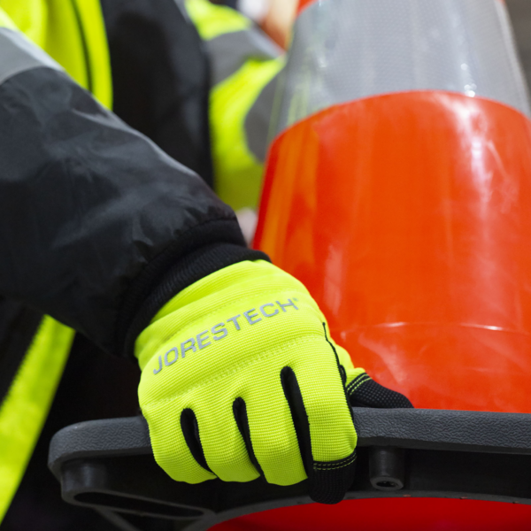 Persona que lleva los guantes de seguridad multipropósito de alta visibilidad mientras transporta un cono de calle