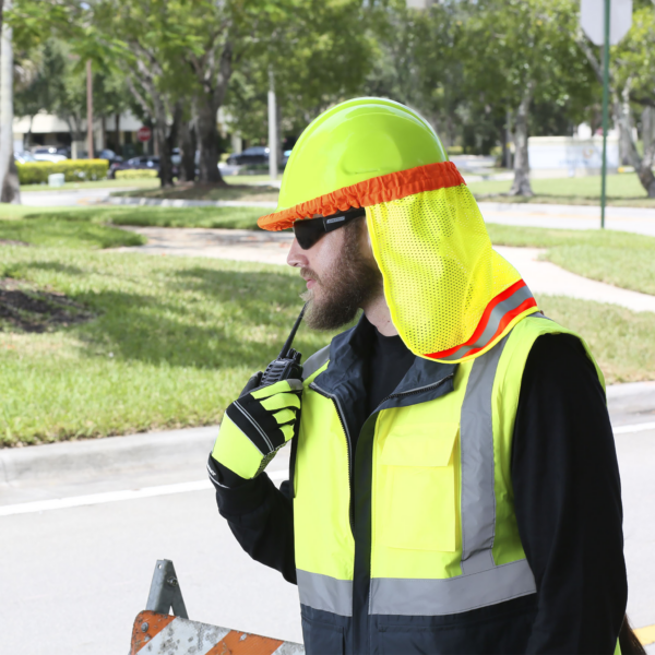 Un hombre lleva un casco de seguridad estilo gorra de color lima con una protección para el cuello JORESTECH de color lima mientras está en una obra en la carretera.