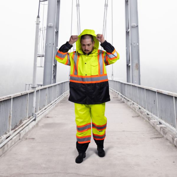 Trabajador usando el conjunto impermeable de seguridad bicolor amarillo en un día nublado sobre un puente.