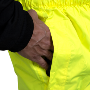 Primer plano que muestra a una persona introduciendo la mano en la abertura de los pantalones impermeables para acceder al bolsillo de los pantalones que lleva debajo