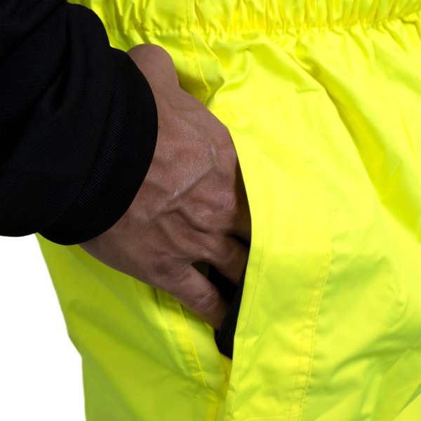 Primer plano que muestra a una persona introduciendo la mano en la abertura de los pantalones impermeables para acceder al bolsillo de los pantalones que lleva debajo