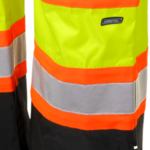 Primer plano de los pantalones impermeables de seguridad amarillos con franjas reflectantes, líneas naranjas en contraste y tejido negro que disimula la suciedad