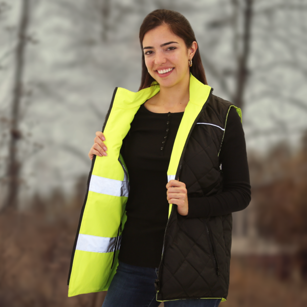 Mujer usando el chaleco de seguridad reversible e insulated JORESTECH amarillo y negro de alta visibilidad con tiras reflectantes, rodeada de árboles durante el otoño