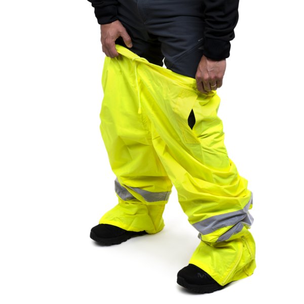Una persona poniéndose los pantalones impermeables de seguridad JORESTECH de alta visibilidad en amarillo con bandas reflectantes