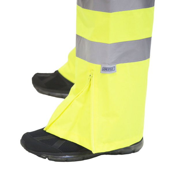 Primer plano de los pantalones de lluvia de alta visibilidad totalmente amarillos/lima ANSI, mostrando la cremallera para ampliar el pantalón y adaptarlo a botas y zapatos
