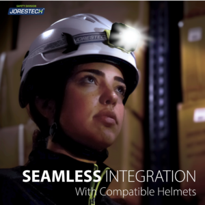 Una mujer lleva un casco de seguridad blanco con una linterna frontal negra compatible. El texto dice: integración perfecta con cascos compatibles. Se encuentra en un entorno donde la fuente principal de luz es la linterna frontal.