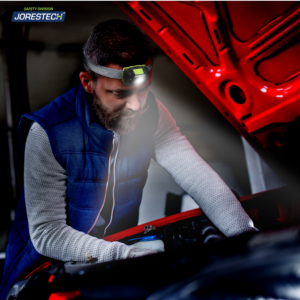 Un hombre que lleva una lámpara frontal LED JORESTECH mientras repara su coche de noche en medio de la carretera.