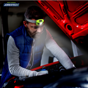 Hombre con una linterna frontal LED JORESTECH mientras da servicio a su coche de noche en medio de la carretera.