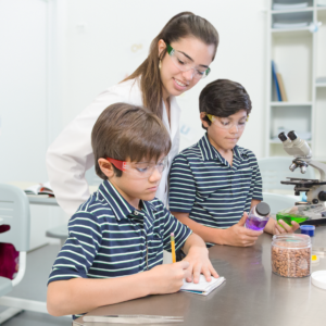 2 niños con uniforme y su profesora en un laboratorio escolar usando gafas de seguridad de alto impacto multicolor JORESTECH