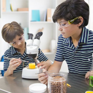 Dos niños llevan gafas de seguridad JORESTECH mientras operan un microscopio en el laboratorio de la escuela