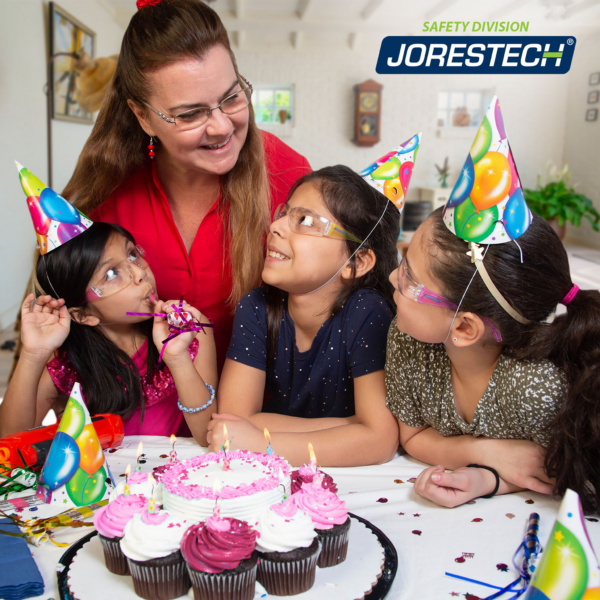 Un grupo de 3 niñas y una madre soplando velas en una fiesta de cumpleaños. Las 3 niñas están sonriendo mientras usan gafas de seguridad multicolor JORESTECH para niños, conformes con ANSI