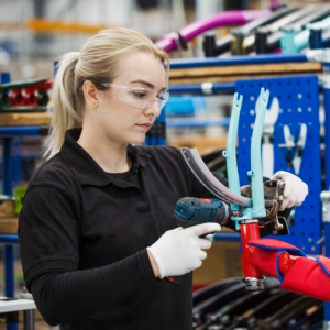 Una mujer lleva las gafas panorámicas de seguridad JORESTECH para protección de alto impacto mientras opera un taladro en un entorno de fabricación