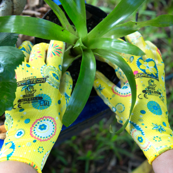 Manos con los guantes de jardinería JORESTECH con palmas recubiertas de nitrilo. La persona está retirando una planta de bromelia de una maceta. Guantes de jardinería JORESTECH encima