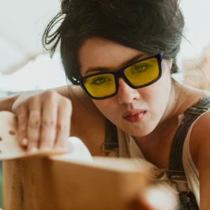 Imagen de una mujer que lleva las gafas de seguridad amarillas JORESTECH con protectores laterales para protección contra impactos fuertes mientras esculpe una gran pieza de madera en un proyecto de bricolaje