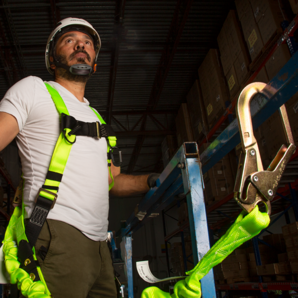 Hombre que lleva un arnés con la eslinga JORESTECH de una sola pata con absorbedor interno de energía, con gancho a presión y gancho para andamios, sujeta a su arnés de seguridad.