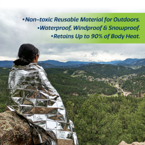 Una persona cubierta con una manta de emergencia color plateado para retener el calor mientras disfruta de la vista desde la cima de una montaña. El texto dice: material no tóxico reutilizable para exteriores. Impermeable, cortaviento y resistente a la nieve. Retiene hasta el 90% del calor corporal.