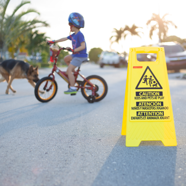El soporte de precaución Jorestech de dos caras y plegable para niños jugando. Hay un niño pequeño montando su bicicleta con su perro a su lado en el fondo