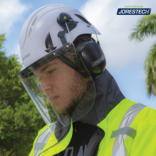 Trabajador usando el sistema de casco de seguridad ventilado para trabajos en altura con protector facial y orejeras. También lleva una chaqueta de seguridad vi-si mientras trabaja al aire libre. Su rostro está protegido por el protector facial JORESTECH