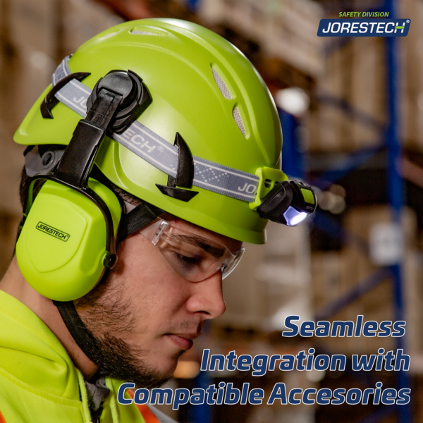 Un hombre en un entorno de almacén lleva el casco de escalada ventilado color lima con un texto azul que dice: Integración perfecta con accesorios compatibles. El casco tiene un soporte para linterna frontal y también un par de orejeras color lima